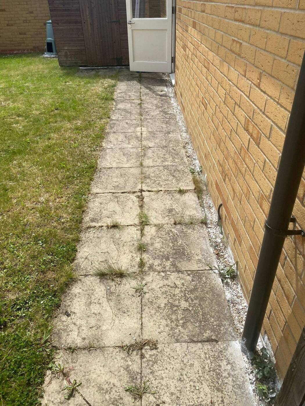 Weathered path slabs alongside house before pressure washing